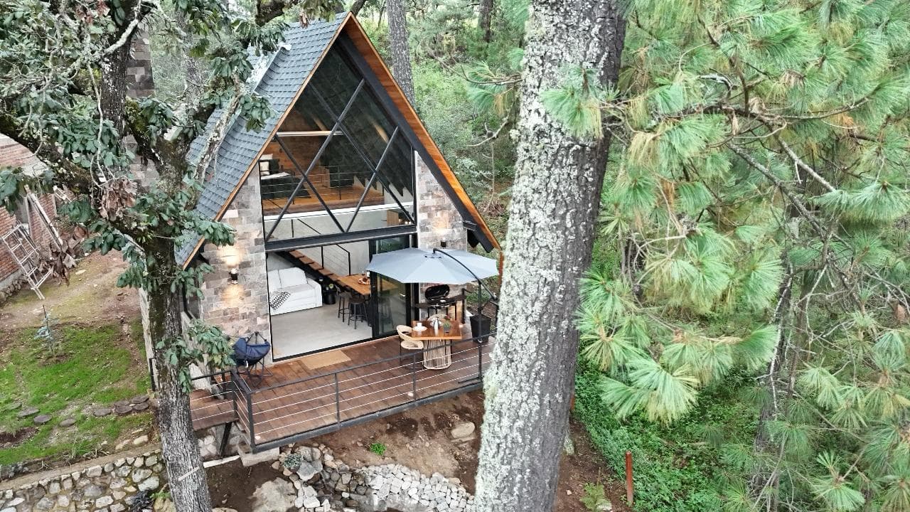 Fachada triangular de piedra, madera y cristal entre el bosque